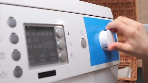 Child Hand Turning Washing Machine Dial on Control Panel Selecting Program and Temperature While