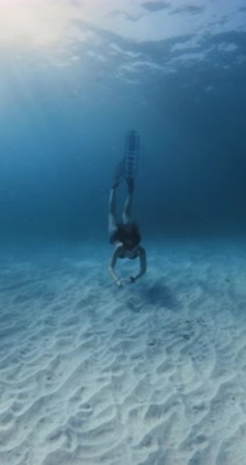 Woman Freediving Underwater in Blue Ocean with Sunshine and Sandy Sea Bottom