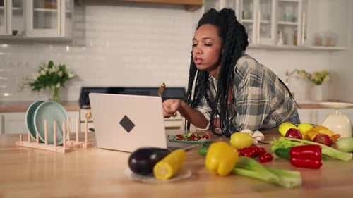 Woman Enjoys Salad While Browsing on Laptop