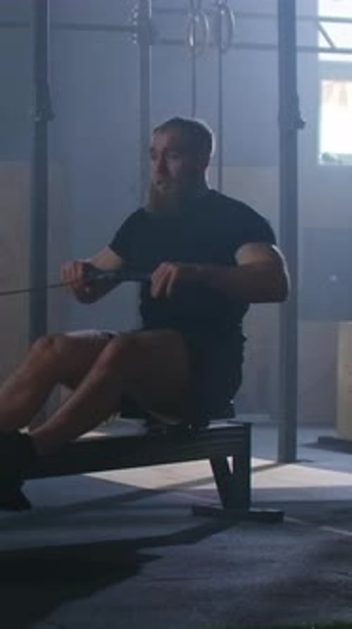 Focused Athlete Performing Intense Indoor Rowing Workout on Exercise Machine in Modern Gym
