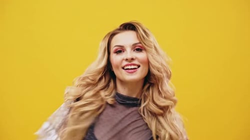 Sexy vollbusige schöne junge blonde Frau tanzt und lacht mit sinnlichen Handgesten über einem gelben