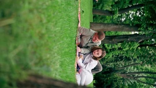 Vertical Video In the Park a Guy and a Girl in Warm Clothes are Resting on a Checkered Blanket