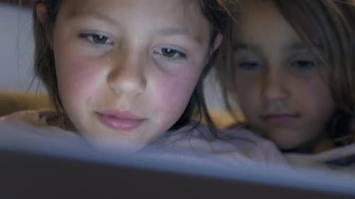 Cinematic close up of two little girls using a tablet or smartphone in the dark. Concept: future o
