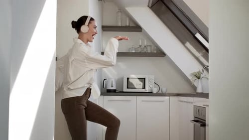 Happy Young Woman Dancing in Kitchen with Headphones