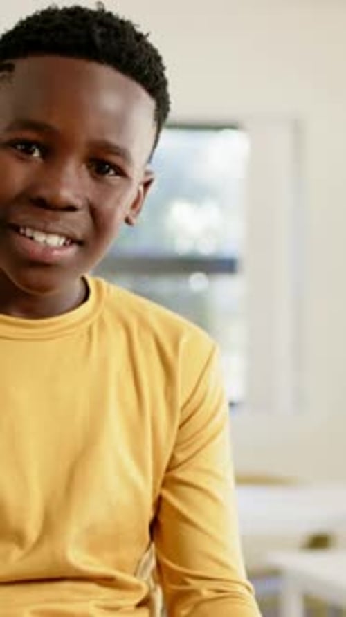 Vertical video: Tapping tablet, teen boy raising head and reacting to camera in study, yellow shirt