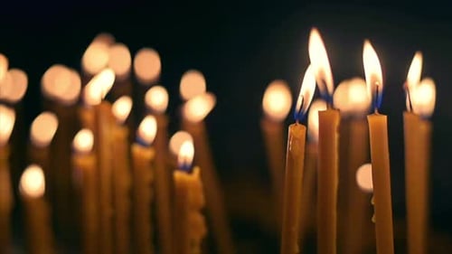 Close view of lots of burning candles with black background. Slow motion