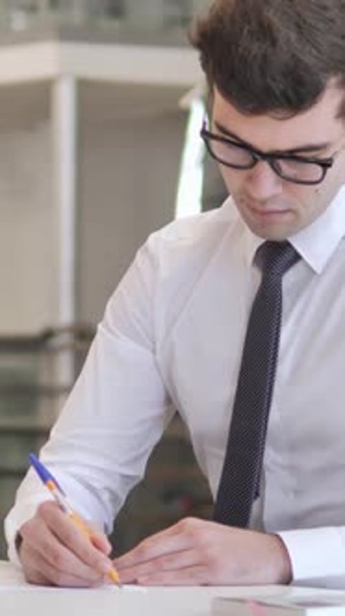 Focused Young Man Writing on Paper in Office