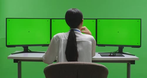 Asian Woman Thinking While Working With Mock Up Multiple Computer Monitor In Green Screen Studio