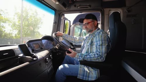 Senior Truck Driver Sitting in Cab Speaks on the Radio Walkie Talkie Right Hand Drive Car
