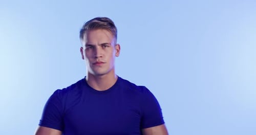 A fit young man posing against a blue studio background