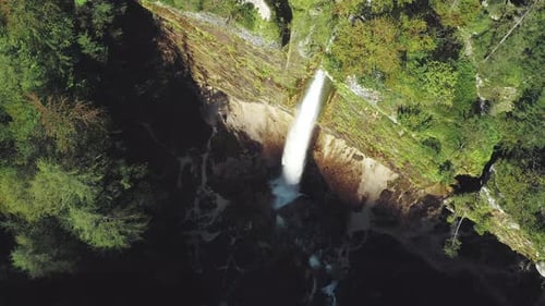 Drone close-up shot of a big waterfall in the mountains surrounded by forest in fall autumn.