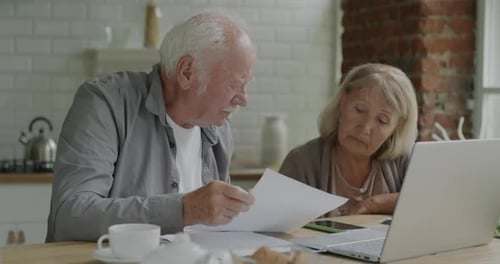 Senior Couple Reviews Documents and Laptop at Home