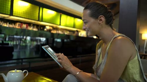 Young woman enjoying coffee and browsing the internet on tablet in a cafe