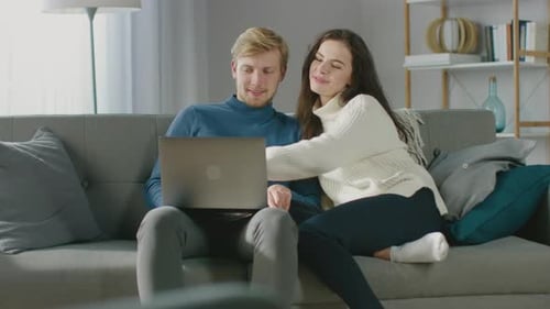 Cheerful Couple Relaxing on Couch Watching Laptop