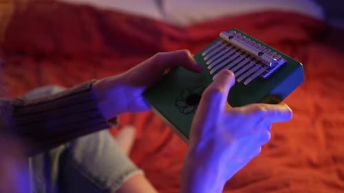Closeup of a Woman's Hands Skillfully Playing a Green Kalimba Illuminated By Soft Blue Light