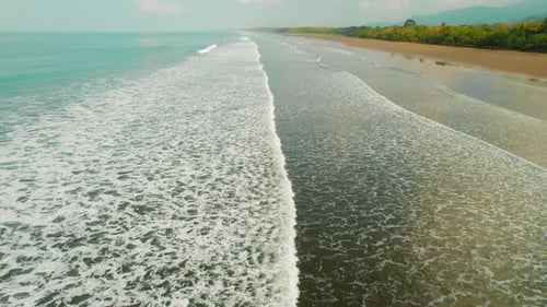 Aerial coastline with ocean waves arriving on a wide sandy beach in Costa Rica