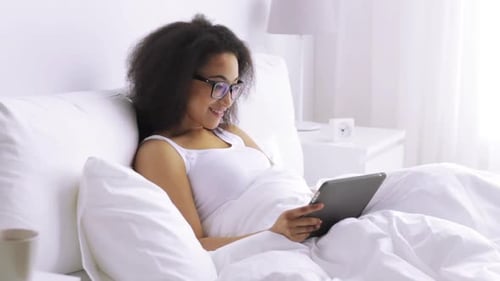 Woman Relaxing in Bed Uses Tablet Device