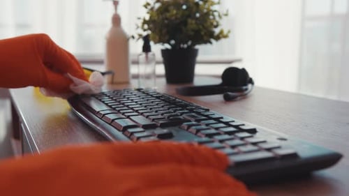 Hands with gloves cleaning a computer keyboard with wipe