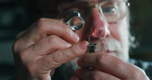 Slow motion close up of experienced goldsmith controlling a quality of precious gem, selected for