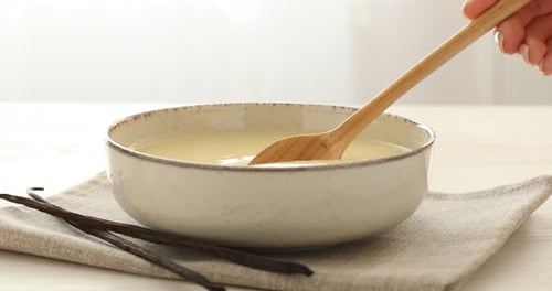 Mujer revolviendo leche condensada de vainilla en un tazón en una mesa iluminada, primer plano