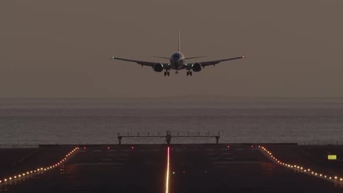 Airplane Landing on Runway Near Ocean at Sunrise