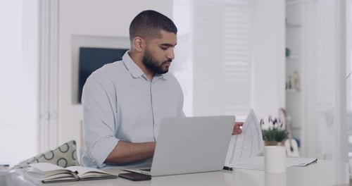 Mixed race businessman looking contemplative, using laptop and reading paperwork in home office