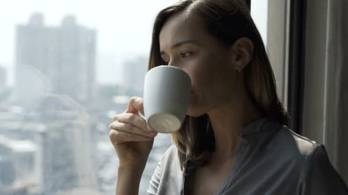 Young Woman Drinking Coffee and Admire View From Window at Home 30s