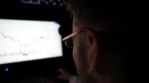 Young Man Works on Computer at Night Profile of Broker Analysing Realtime Stocks Commodities and