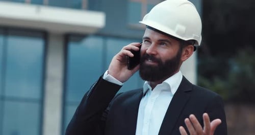 Businessman in Hard Hat Actively Talking on the Phone on Construction Background Profession Concept