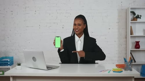 Woman Holds Up Phone with Green Screen at Desk