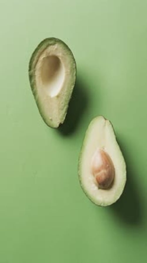 Vertical video of sliced avocado with copy space over green background