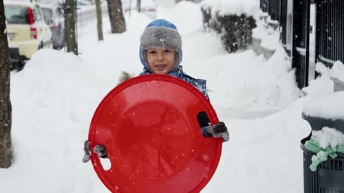 Câmera lenta de menino alegre andando com trenós de plástico na queda de neve no parque de inverno