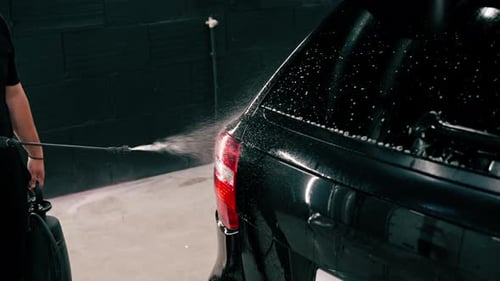 close-up A male car wash employee applies car wash detergent to a black luxury car using spray gun