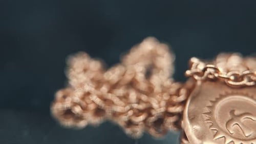 A smooth detailed tilt down shot of a golden medallion necklace, flying bird in the middle of the su