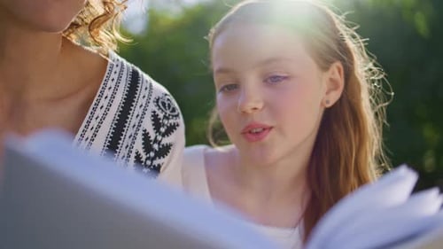 Smiling Girl Reads Book with Mother Outdoors
