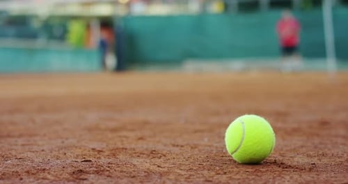 Tennis Ball Sits on Clay Court, Player Practices