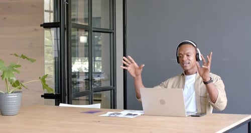 Using laptop and wearing headphones, man having video conference in modern office