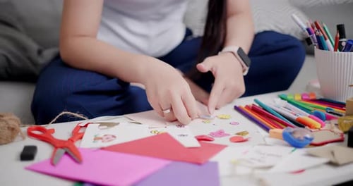 Close-up of young woman's hands making a greeting card in the living room at home.
