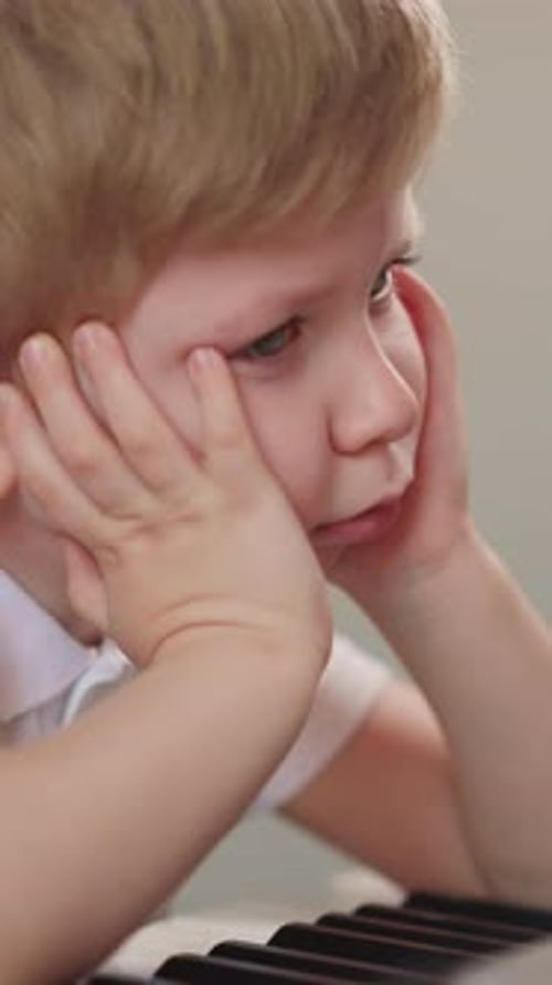Little Boy Leans on Hands and Breathes Out Sadly at Piano