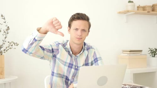 Thumbs Down By Young Man Working on Laptop in Office