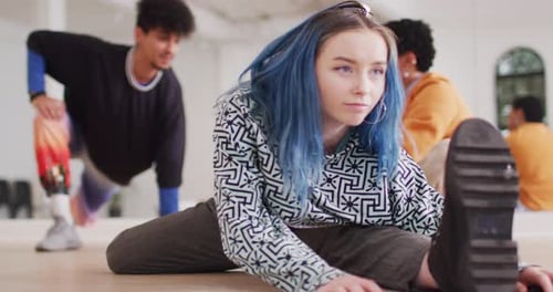 Caucasian female dancer stretching with diverse colleagues in dance studio, slow motion