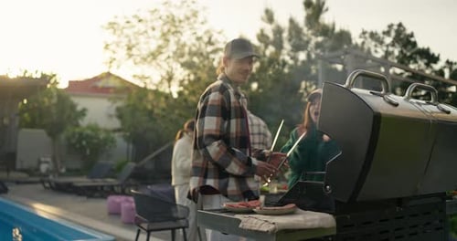 Man Grilling Outdoors Beside a Pool at Sunset