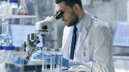 Serious Man Using Microscope in a Bright Lab