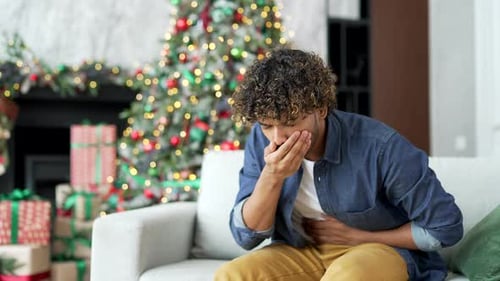 Young handsome man suffering from nausea, wants to vomit sitting on sofa in living room at home