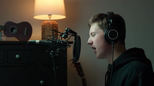 Young man recording vocals in a cozy home studio with headphones, professional condenser microphone