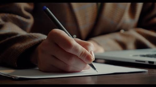 Close-up of a businesswoman in a blazer writing notes on a sheet of paper with a pen
