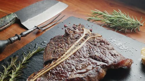 T-Bone-Steak mit Kräutern und Knoblauch auf dem Servierbrett in Nahaufnahme.