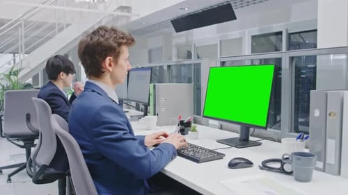 Young Handsome Manager in a Suit Works on a Desktop Computer with Green Screen Mock Up. Diverse and