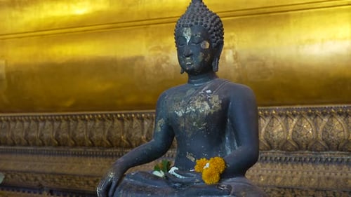Seated dark Buddha statue with golden leaf in Wat Pho, Bangkok