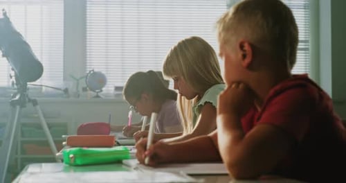 Primary School Children Sitting at Desks Writing School Exam or Doing Tasks in Notebooks